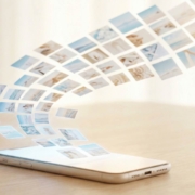 004- TMB Blog Post- Featured-Image-2 Photos flowing upward from a smartphone screen into an organized grid pattern, illustrating automatic cloud backup and photo organization