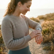 Person checking their smartwatch during an outdoor walk in natural coastal setting, illustrating health and activity tracking in a wellness context