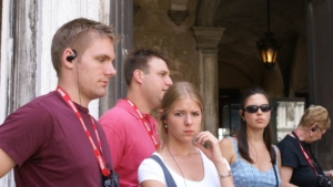 Tour group members wearing earpieces and tour company lanyards in Italy, illustrating the traditional guided tour experience